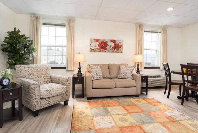 A cozy living room with a sofa, armchairs, and a colorful rug beneath soft lighting.