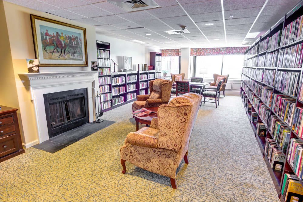 A cozy library with armchairs, a fireplace, and bookshelves lining the walls.