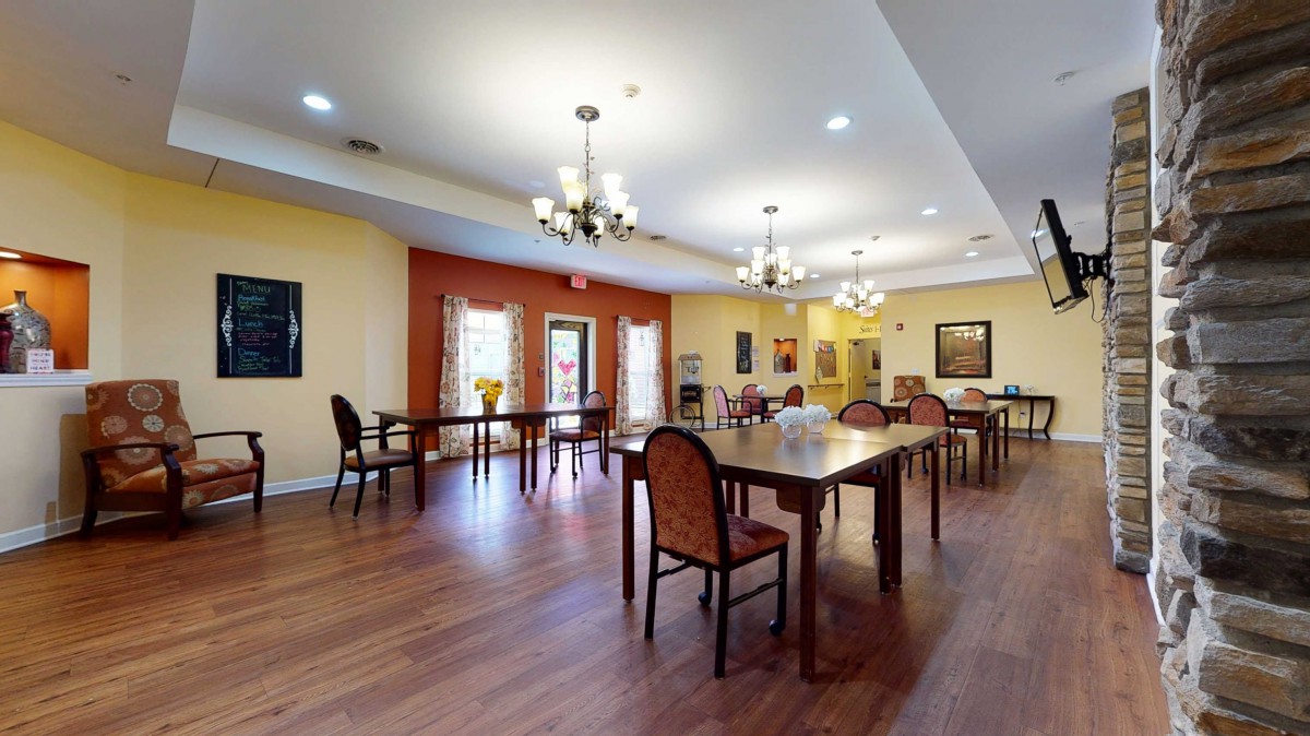A spacious dining area with wooden floors, decorated with chandeliers and arranged with tables and chairs.