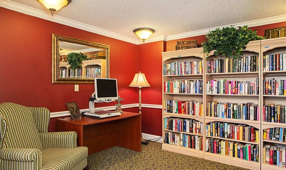 A cozy home office with a computer desk, bookshelf, and armchair.