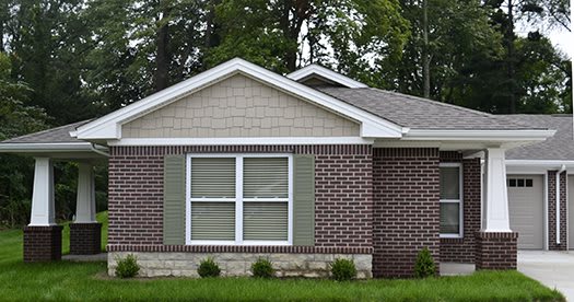 A suburban brick house with green shutters and neatly trimmed lawn.