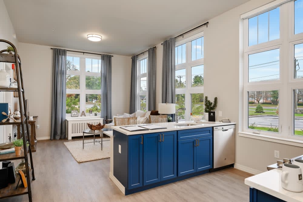 A modern open floor plan features a kitchen with blue cabinets and abundant natural light from large windows.