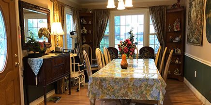 A cozy dining room with a floral tablecloth, chairs, and a centerpiece of flowers.