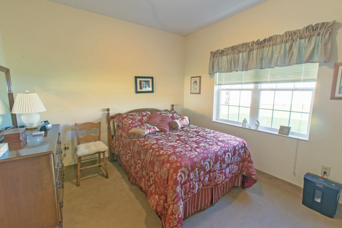A cozy bedroom with a patterned bedspread and natural light coming through the window.
