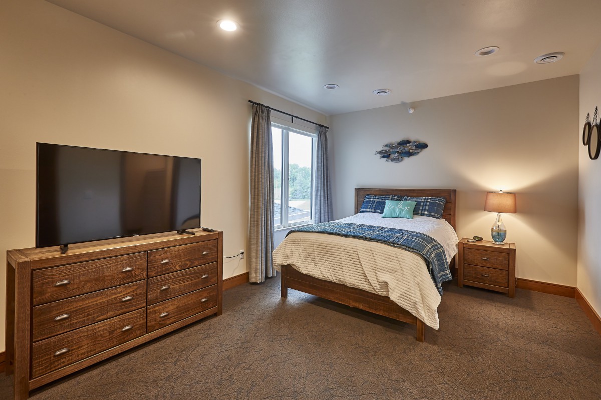 A cozy bedroom with a neatly made bed, wooden dresser, and a flat-screen TV.
