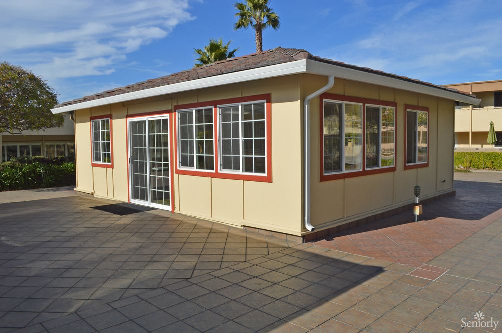 A small building with large windows and a patio area, surrounded by palm trees on a sunny day.