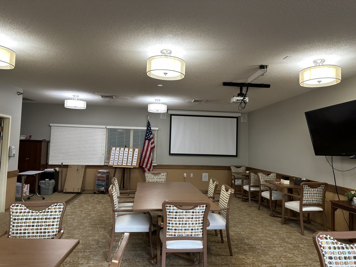 A well-lit conference room featuring a projector screen, tables, chairs, and an American flag.