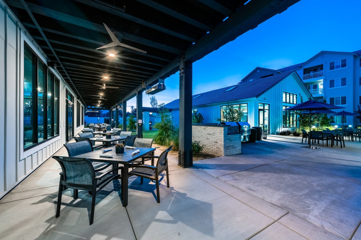 A modern outdoor restaurant patio in the evening with tables, chairs, and ambient lighting.