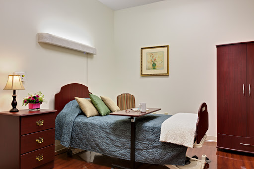 A cozy hospital room featuring a bed with pillows, a table, and decorative wall art.