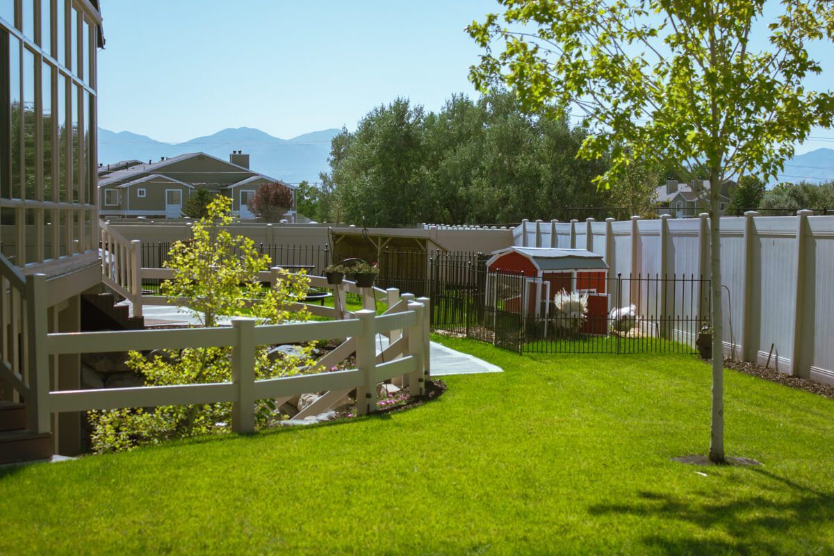 A tranquil backyard garden with lush green grass, a wooden fence, and scenic mountain views on a sunny day.