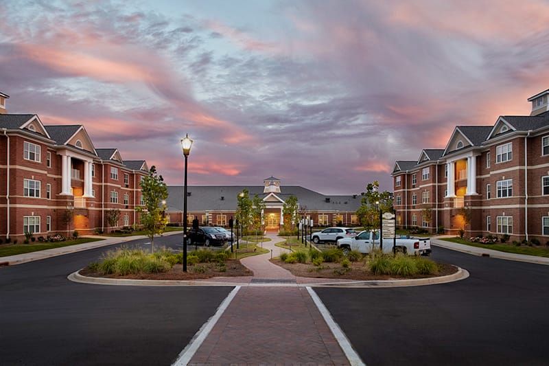 A modern building with a parking lot at sunset, featuring street lamps and a clear pathway.