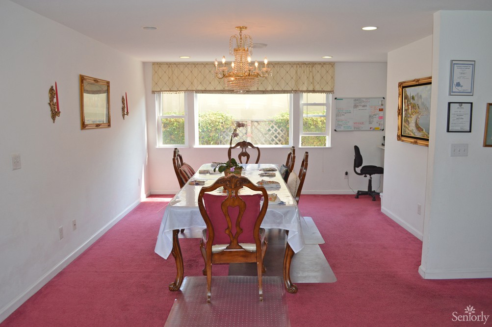 Elegant dining room with a chandelier, set table, and pink carpet.