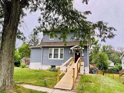 A charming two-story house with a wooden accessibility ramp and a well-maintained front yard.