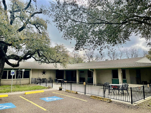 A modern building surrounded by trees, featuring a parking lot and a cloudy sky.