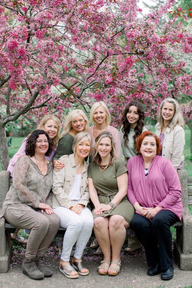A group of women posing together in front of blossoming trees.