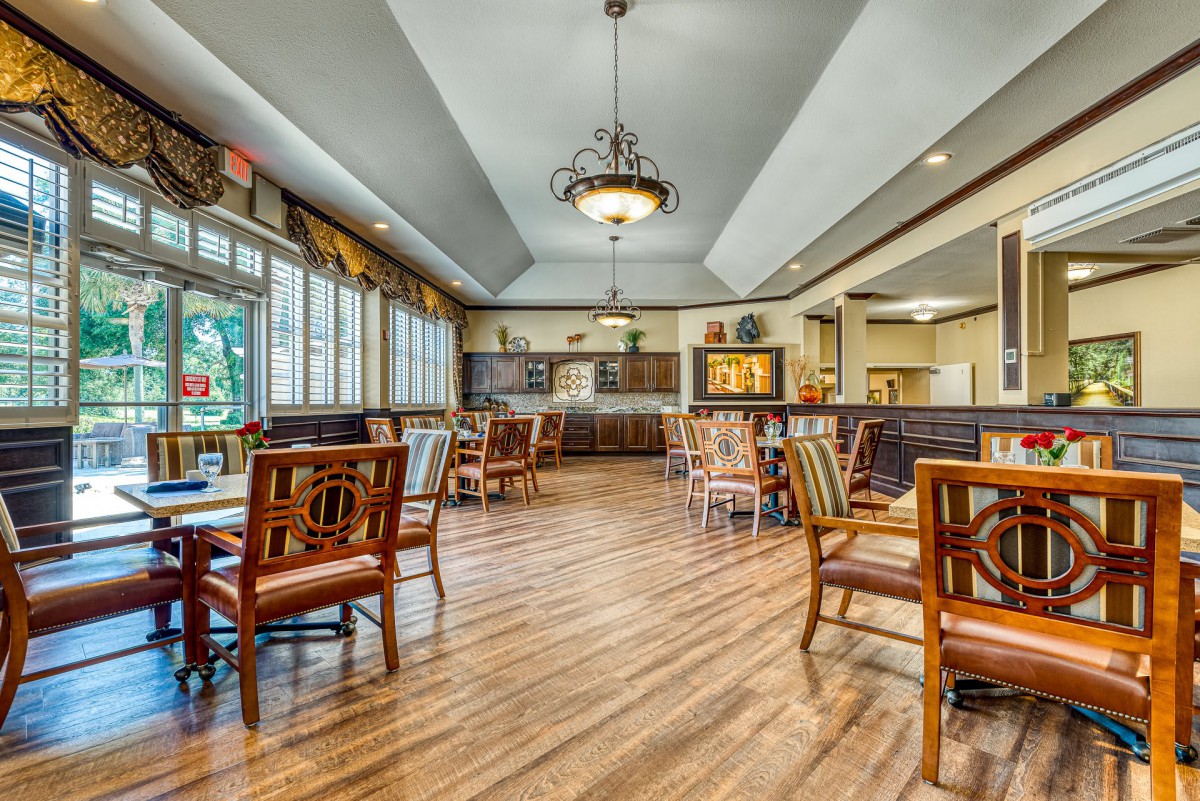 A spacious dining area with wooden floors, tables, and chairs, illuminated by a chandelier.