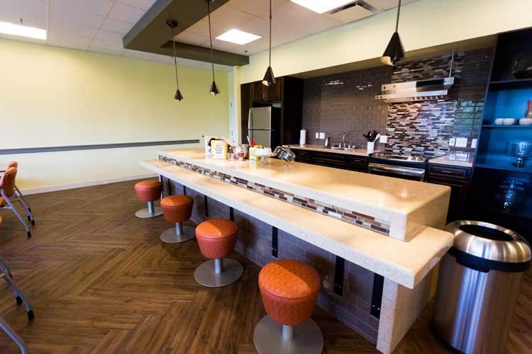 A modern kitchen with a sleek countertop and orange stools.