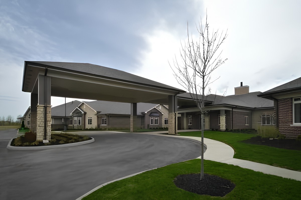 A suburban building with a covered driveway and landscaped area under an overcast sky.