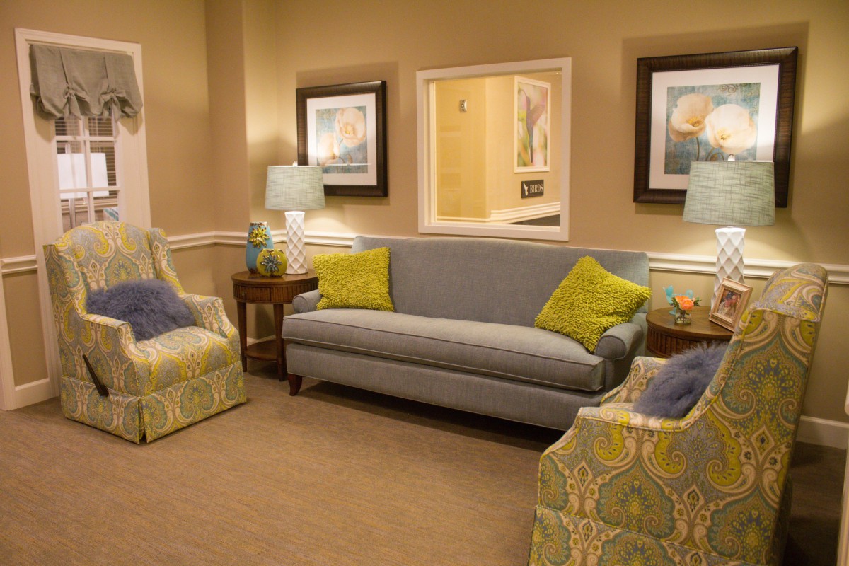 A cozy living room with a sofa, two patterned chairs, and decorative cushions, illuminated by table lamps and accented with framed art.
