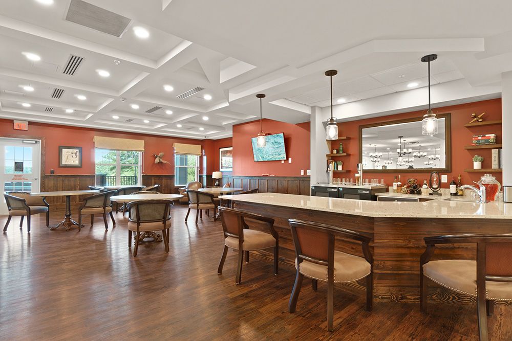 A spacious dining area with wooden floors, tables, and chairs, featuring a bar counter and stylish lighting.