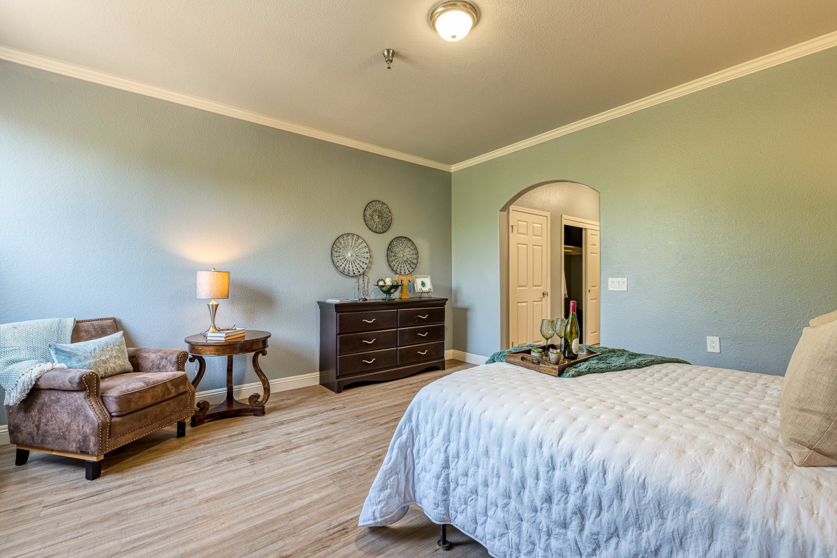 A cozy bedroom featuring a bed with white bedding, a dresser, and warm lighting from a lamp on a side table.