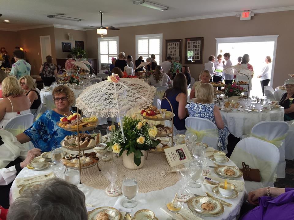 A lively indoor gathering with elegantly set tables and guests enjoying a tea party.
