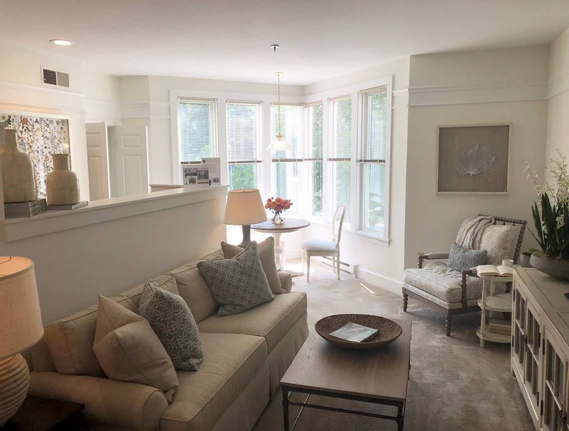 A cozy living room with natural light, featuring a sofa, armchair, and dining area.