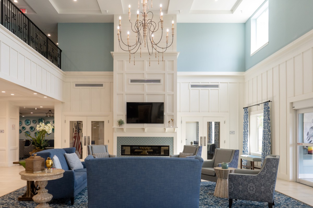 A spacious living room with a large chandelier, blue sofas, and a fireplace under a high ceiling.