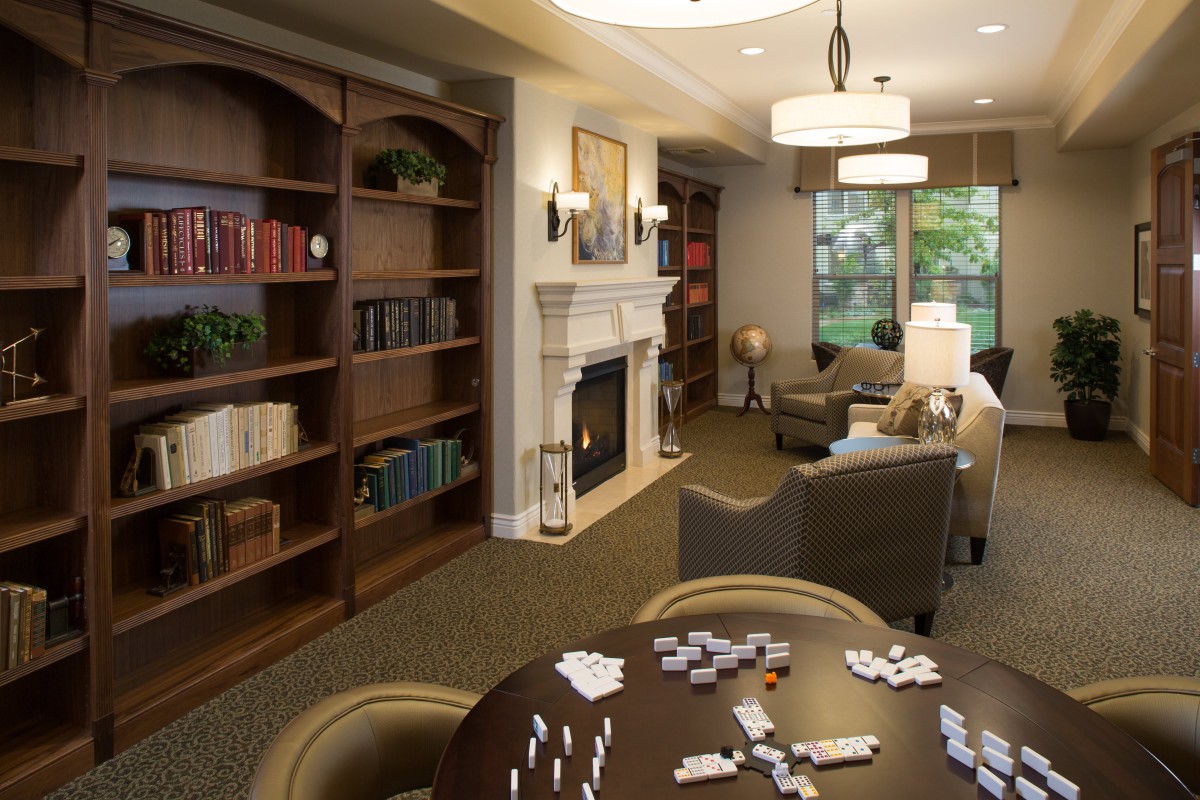 A cozy library space with bookshelves, a fireplace, and a game table with dominoes.