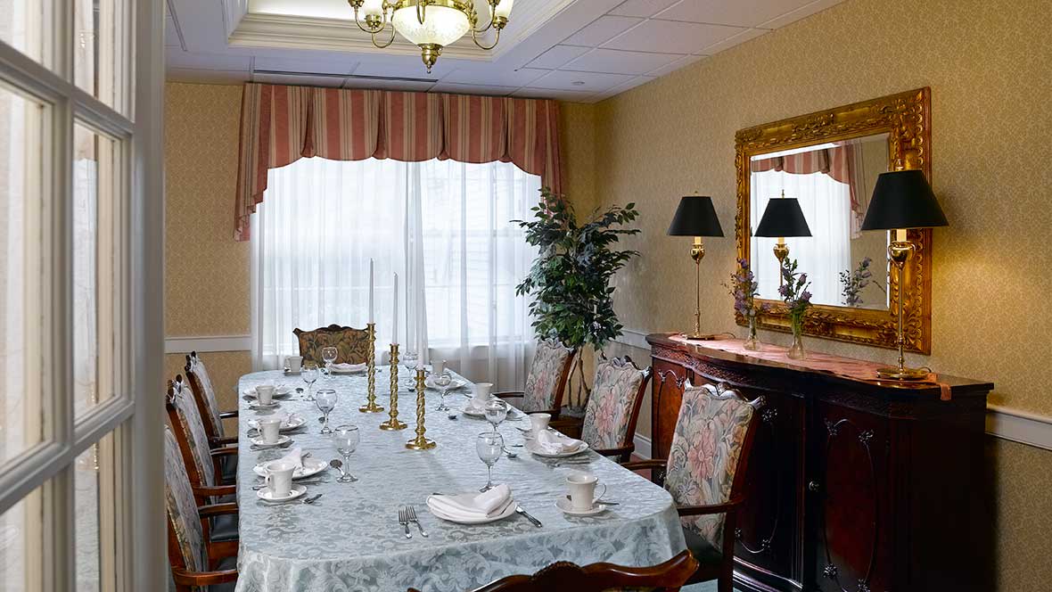 An elegantly set dining room featuring a long table with candlesticks, surrounded by ornate chairs and illuminated by a chandelier.