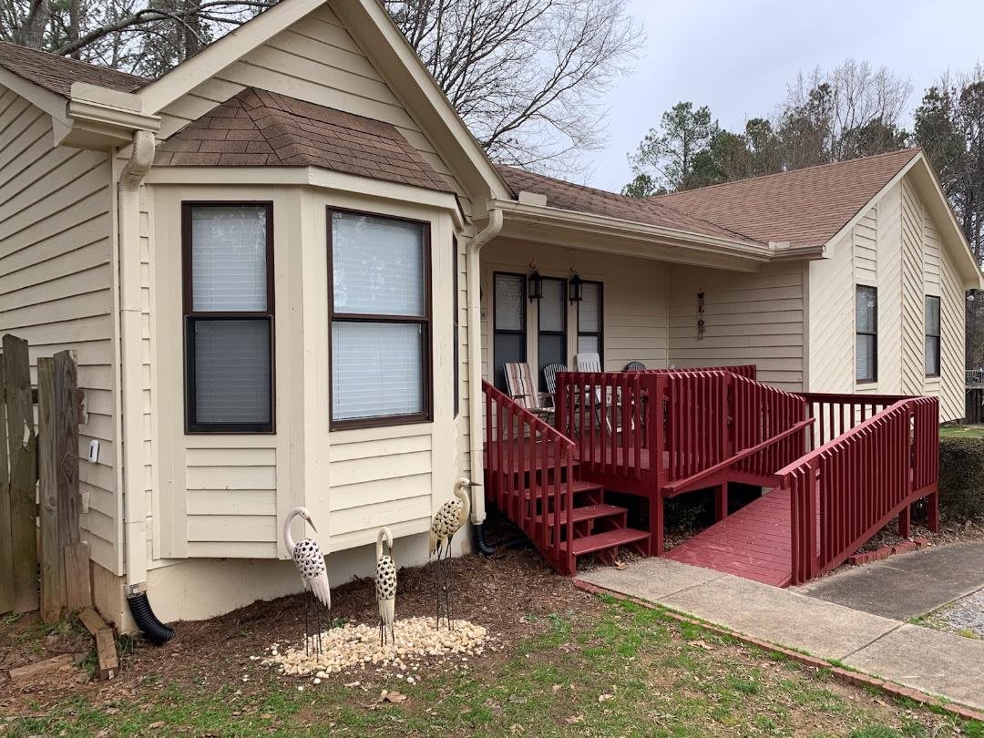 A residential house with a red porch and ramp, featuring multiple windows and a small yard.