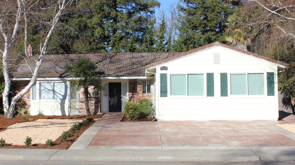 A single-story suburban house with a paved driveway and surrounding trees.
