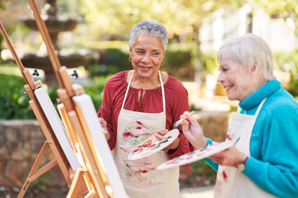 Two senior women enjoying painting together outdoors.