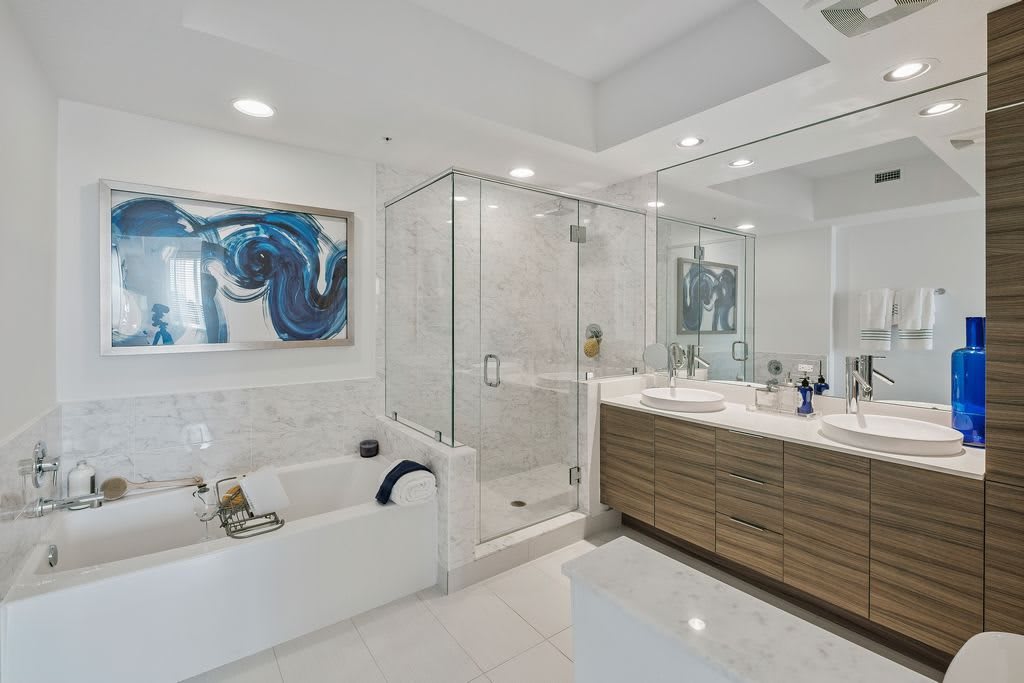 A modern bathroom featuring a glass shower, bathtub, and stylish vanity with contemporary art on the walls.