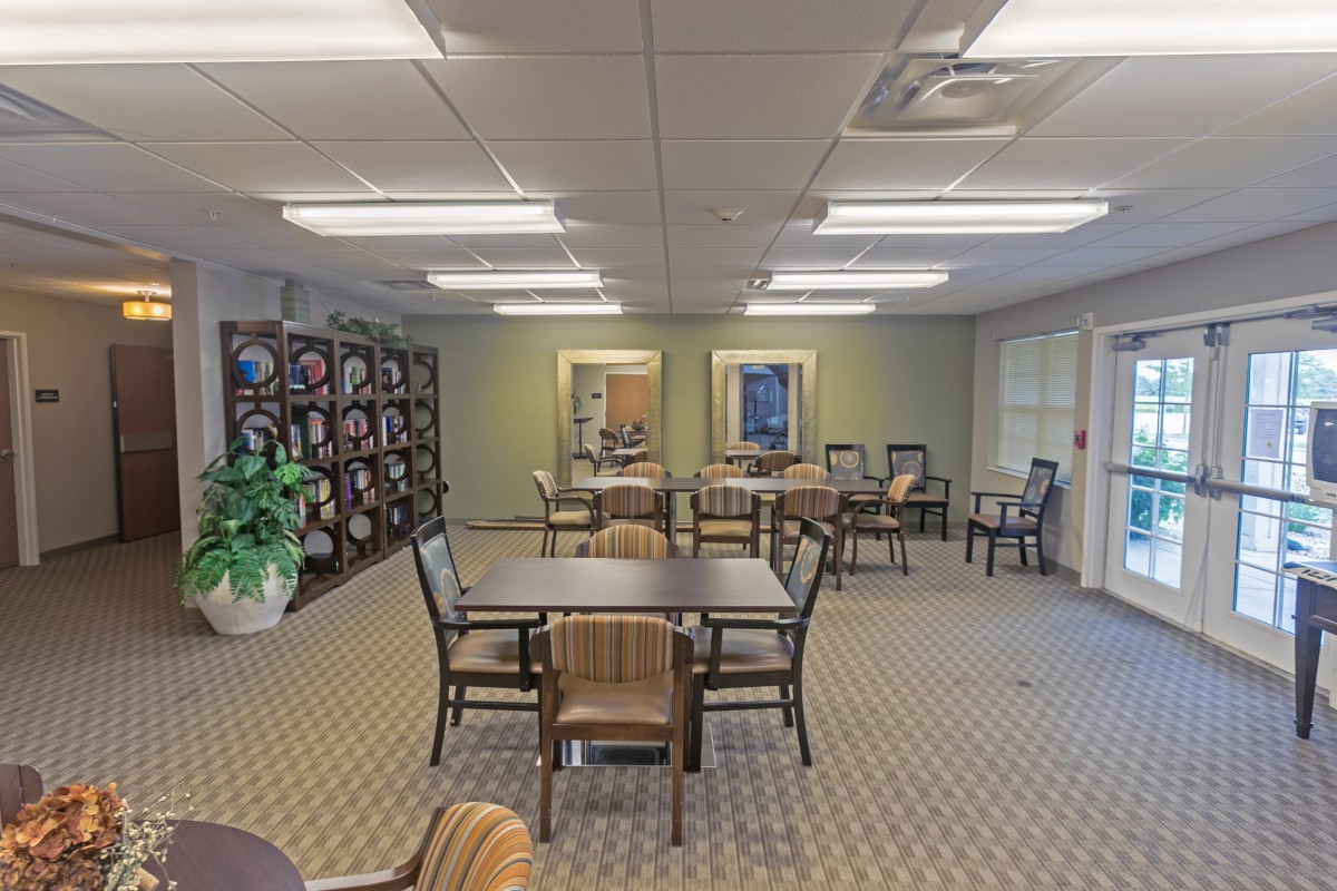 A well-lit dining area with multiple tables and chairs arranged neatly on a carpeted floor, featuring decorative elements and plants.