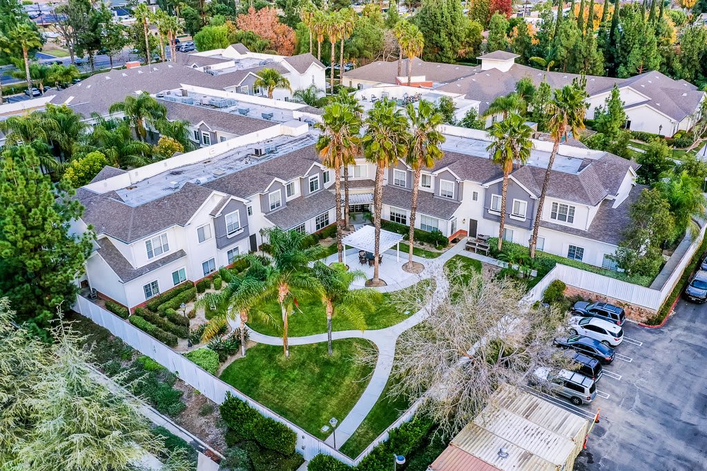 Aerial view of a residential complex surrounded by lush gardens and palm trees.