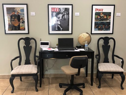 A cozy office space featuring a desk with a computer, two elegant chairs, and framed magazine covers on the wall.