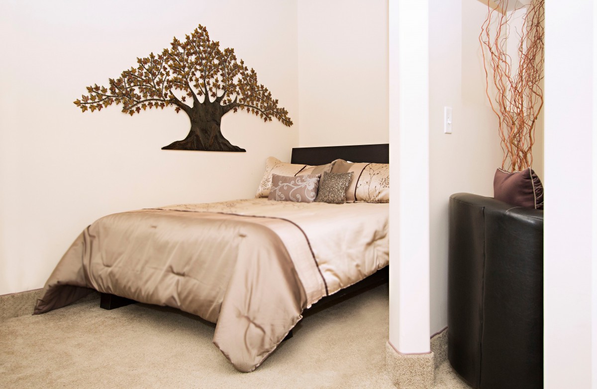 A cozy bedroom features a decorative tree wall art above the bed and elegant bedding.