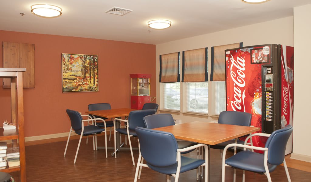 A cozy dining area with tables, chairs, a vending machine, and artwork on the wall.