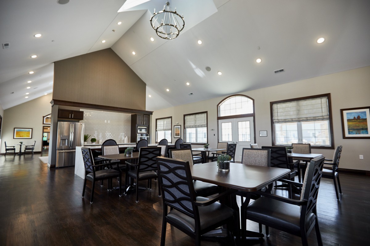 A modern dining room with multiple tables and chairs, featuring a kitchen area and contemporary lighting.