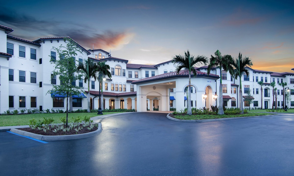 A grand building with a circular driveway and palm trees at sunset.