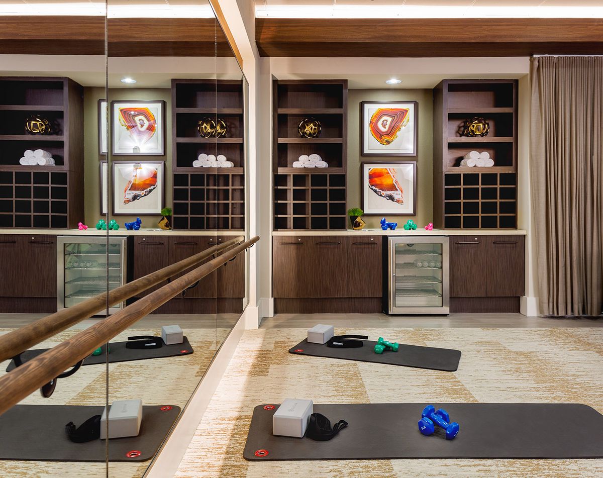 A well-equipped yoga room with mats, blocks, and resistance bands in front of mirrored walls and artwork.
