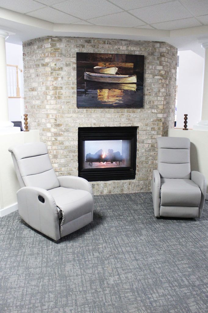 A cozy living room setup featuring two modern armchairs in front of a stone fireplace, complemented by a decorative painting above.
