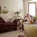 An elderly woman reading a book in a cozy living room.