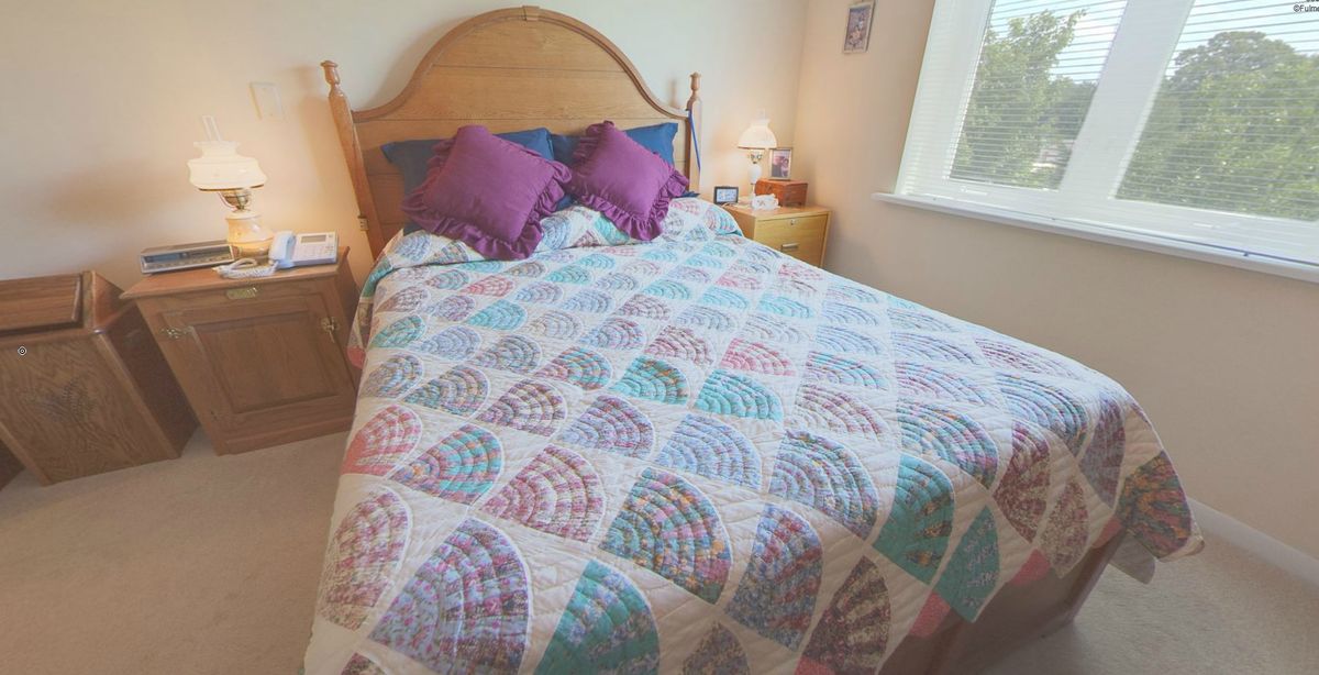 A cozy bedroom featuring a colorful quilt with geometric patterns and purple pillows.