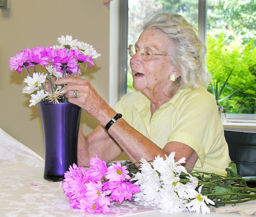 An elderly woman carefully arranges beautiful flowers in a vase, showcasing her love for floral design.