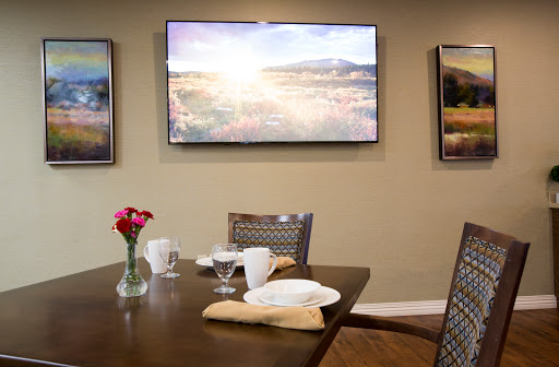 A cozy dining area featuring a neatly set table, wall art, and a television displaying a scenic view.