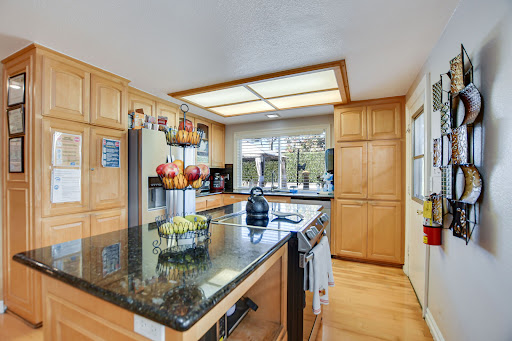 A modern kitchen featuring wooden cabinets, a black granite countertop, and ample natural light.