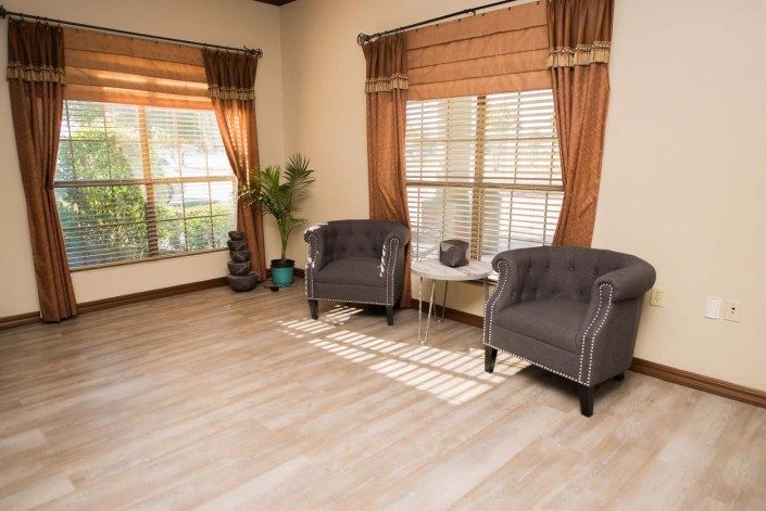 A cozy living room with two upholstered chairs and large windows, complemented by warm curtains and wooden flooring.