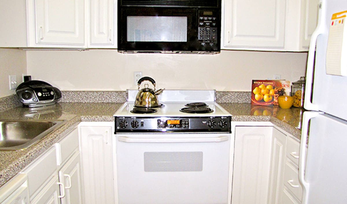 A kitchen stove with a teapot, beneath a microwave and next to a box of oranges on the countertop.